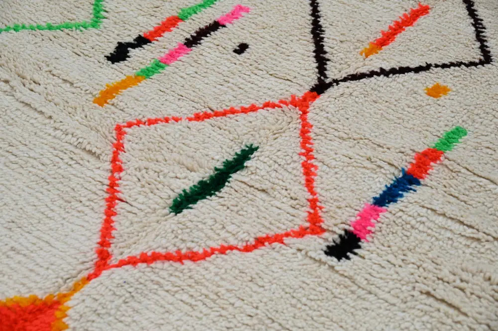 Cream-colored moroccan azilal rug with vibrant red green black and orange geometric patterns made of natural wool