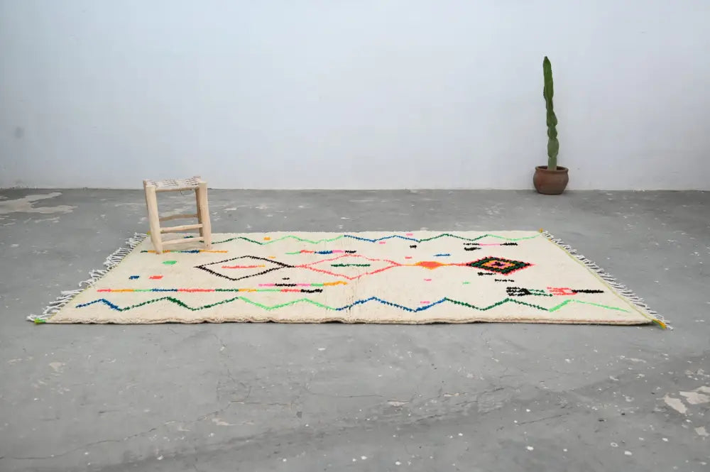 Cream-colored moroccan azilal rug with vibrant geometric patterns in pink green blue and orange on natural wool base