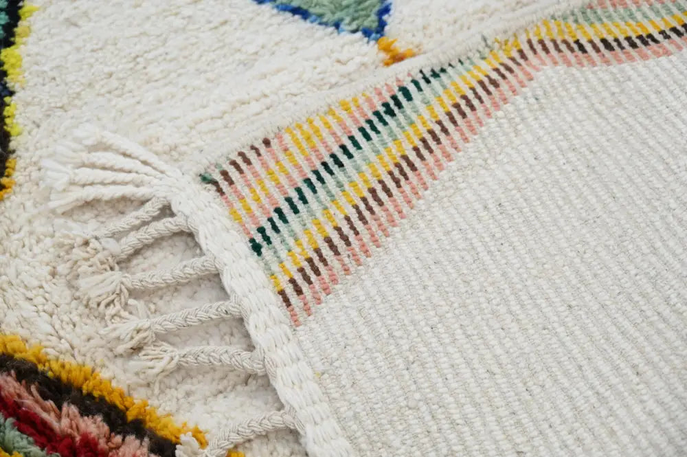 Cream-colored handmade moroccan azilal rug with textured weave and colorful geometric patterns along fringed edge