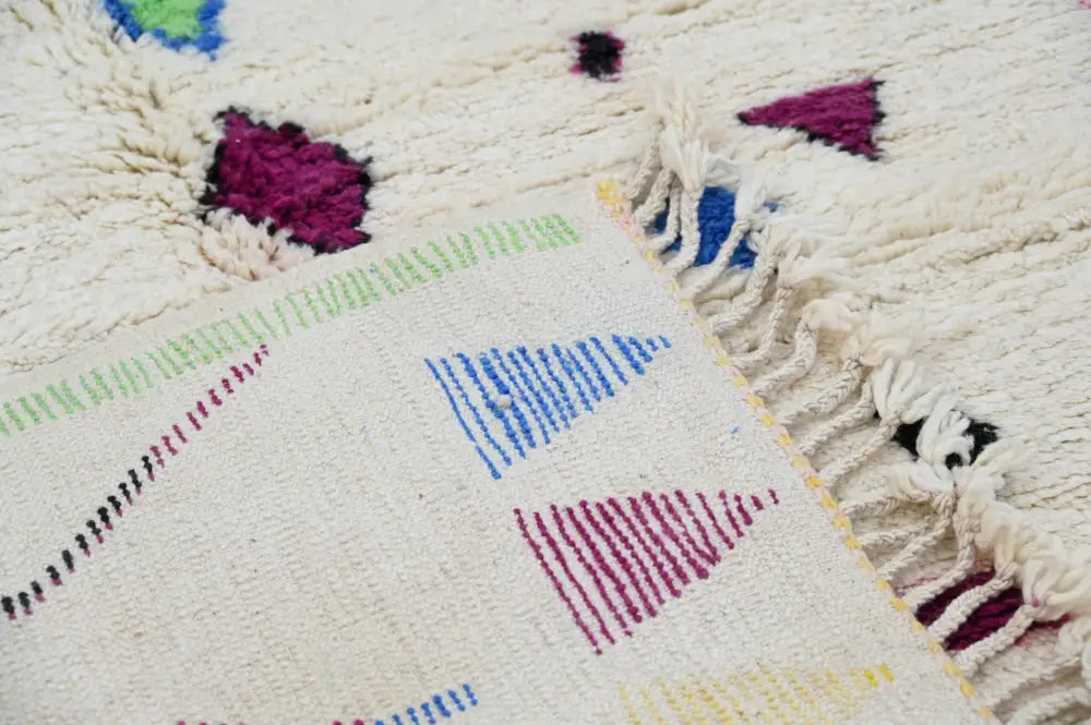 Cream-colored handmade moroccan azilal rug with vibrant colors and geometric patterns on textured woolen surface