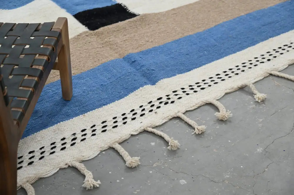 Cream-colored handmade traditional azilal rug with blue beige and black geometric stripes and tassels showcasing moroccan craftsmanship