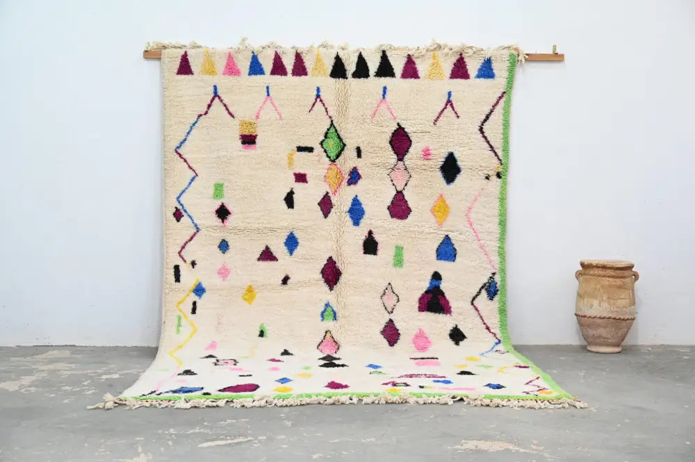 A vibrant cream-colored handmade Moroccan Azilal rug with colorful geometric patterns in pink green blue and purple