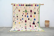 A vibrant cream-colored handmade Moroccan Azilal rug with colorful geometric patterns in pink green blue and purple