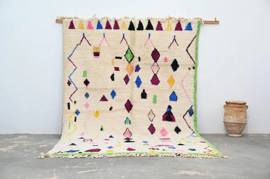 A vibrant cream-colored handmade Moroccan Azilal rug with colorful geometric patterns in pink green blue and purple