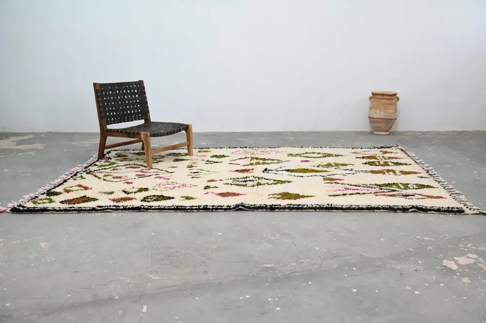 Cream-colored handmade moroccan azilal rug with geometric botanical patterns in muted greens pinks and browns with black fringe