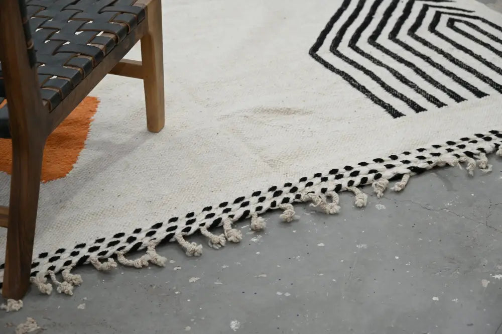 A cream-colored handmade moroccan azilal rug with black geometric pattern and tasseled edges 308x200 cm