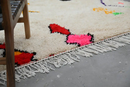 DecorBites™ handmade Moroccan Azilal rug with bold red and pink geometric patterns and white fringe on cream background