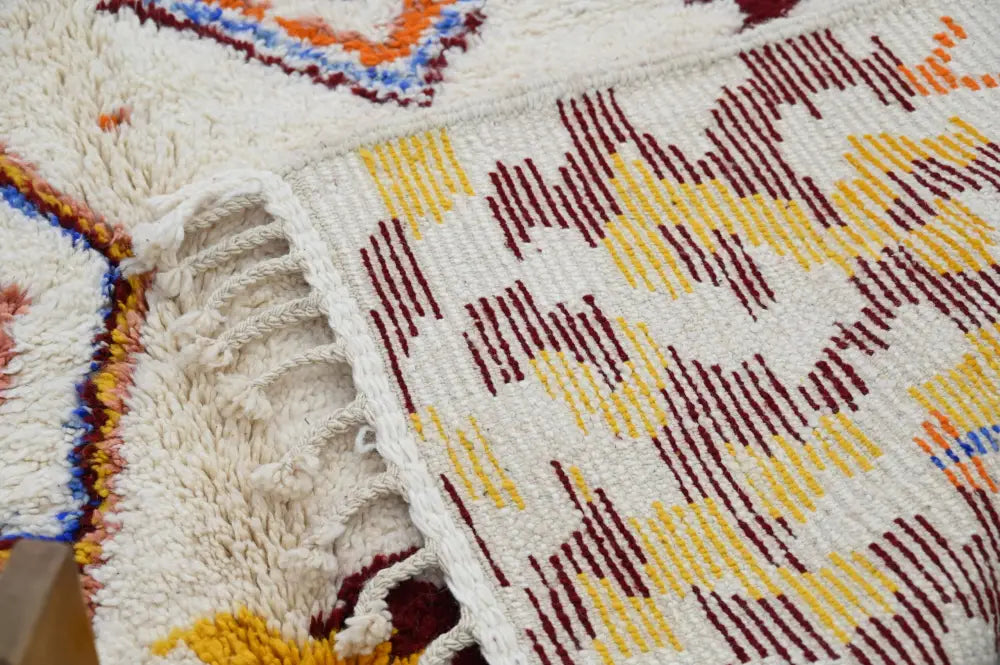 A cream-colored handmade moroccan azilal rug with maroon yellow and blue geometric threads 309x207cm