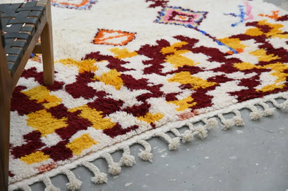 DecorBites™ handmade Moroccan Azilal rug with vibrant maroon and mustard geometric pattern on cream background with tassels