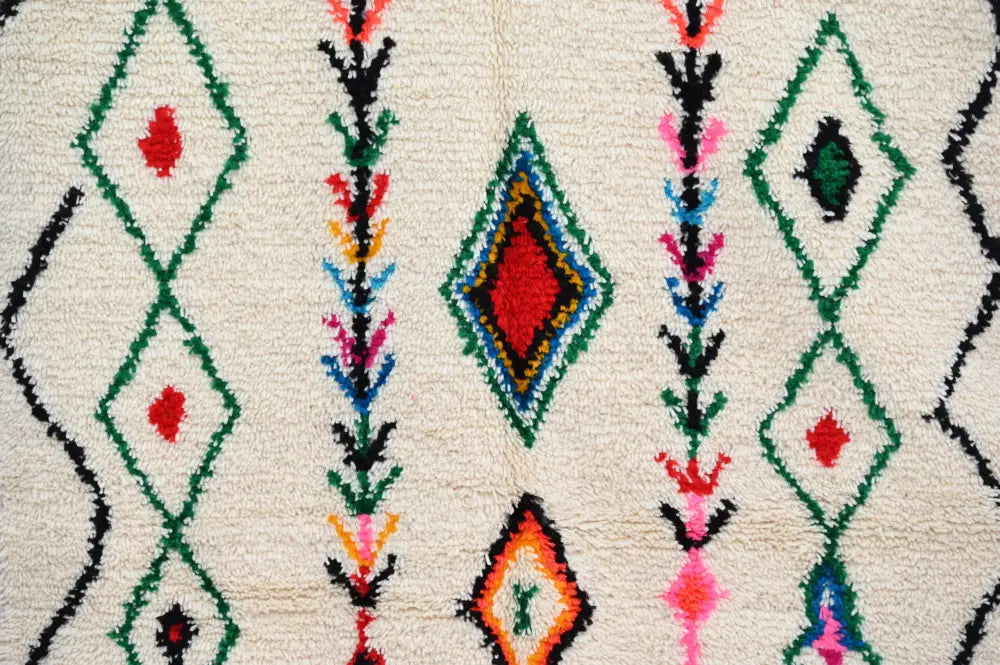A cream-colored decorbites handmade traditional azilal rug with vibrant green red black geometric and floral patterns