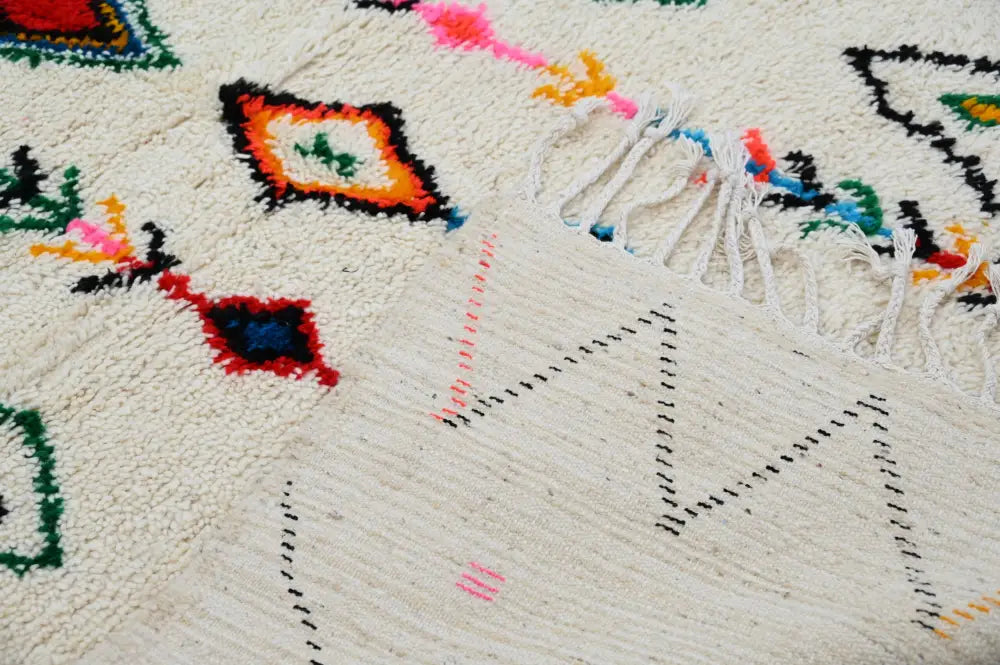 Cream-colored decorbites™ handmade traditional azilal rug with vibrant geometric patterns and fringed edges 240x150cm