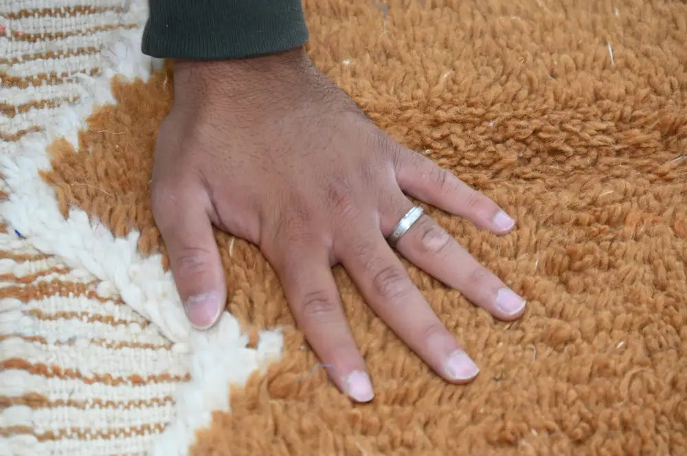 A simple silver band ring worn on a finger alongside a traditional azilal rug by decorbites measuring 328x197cm