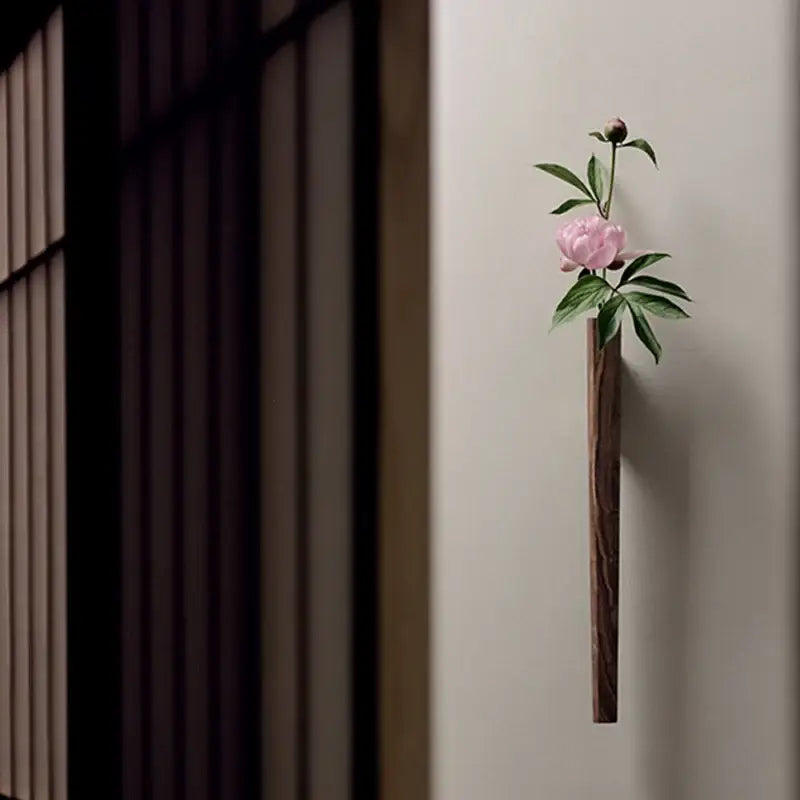 DecorBites™ handmade nordic wall vase in dark solid wood holding a pink peony with green leaves
