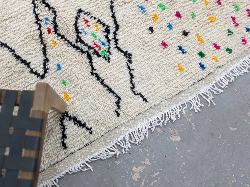 Cream-colored decorbites™ handwoven moroccan azilal rug with black geometric patterns and colorful embroidered dots