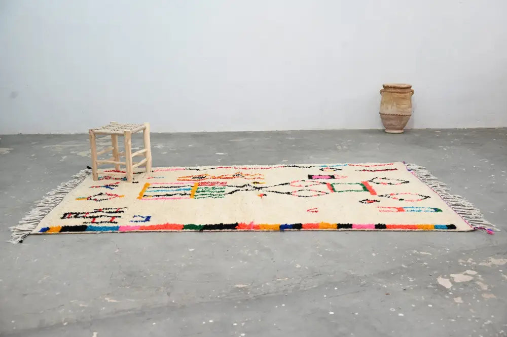 Cream-colored handwoven Moroccan Azilal rug with vibrant geometric patterns and fringed edges 245x146 cm DecorBites