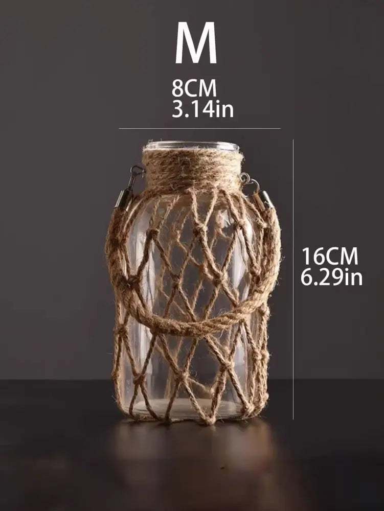 A clear glass hanging vase with woven jute netting and metal clasps featuring hemp rope for rustic decor