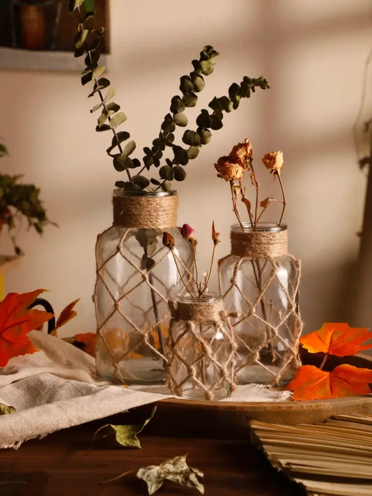 Three clear hanging glass vases with hemp rope wrapped necks and intricate twine netting for rustic home decor