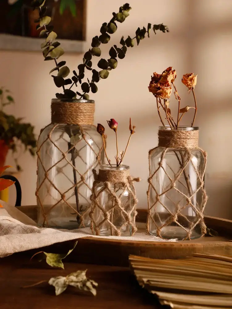 Three clear glass hanging vases wrapped with rustic hemp rope holding dried botanicals for home decor