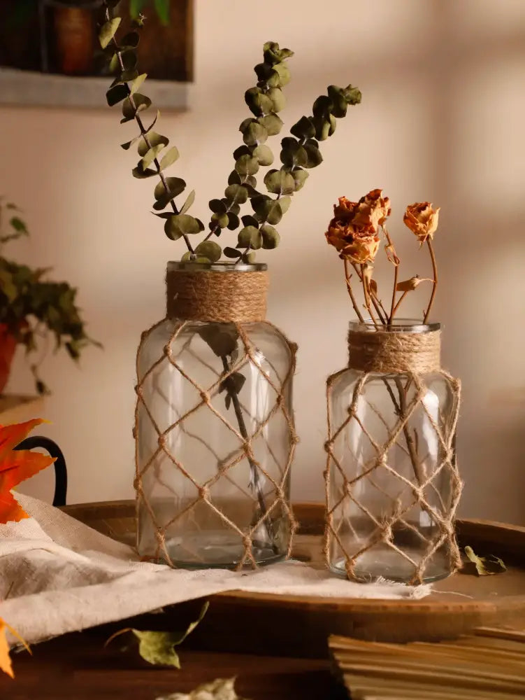 Two clear hanging glass vases wrapped in rustic hand-woven jute netting with hemp rope for rustic home decor
