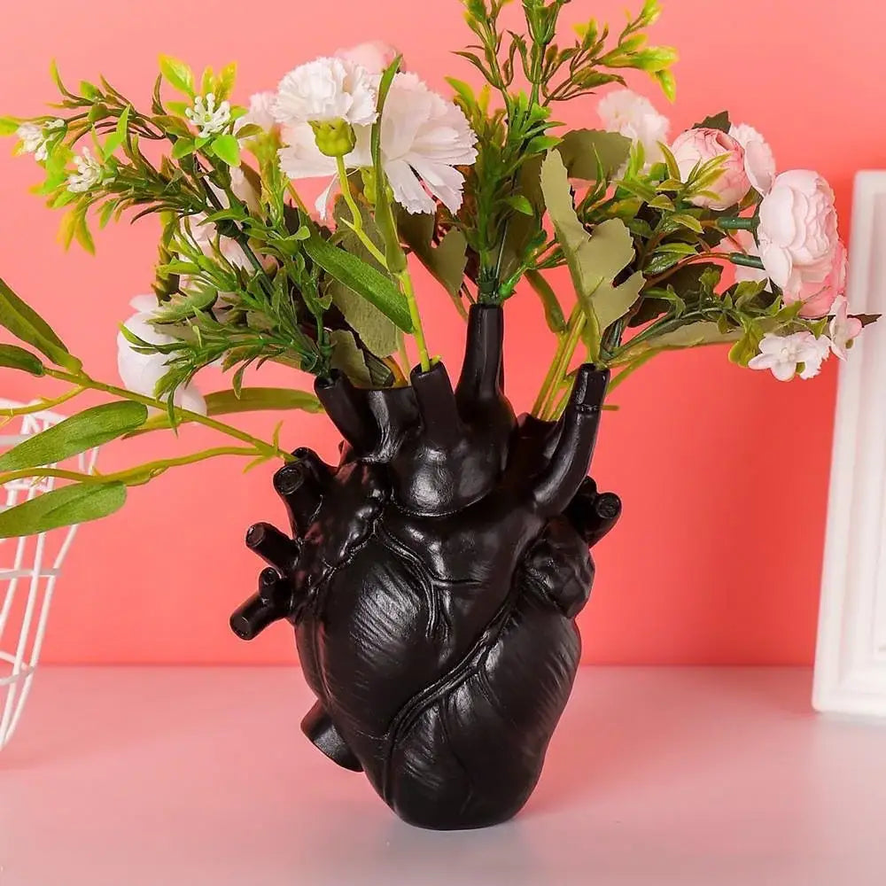 Black anatomically detailed heart shape resin vase holding artificial white and pink flowers by DecorBites