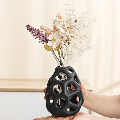 Black ceramic vase with geometric cutouts holding dried flowers featuring nordic classical design by decorbites