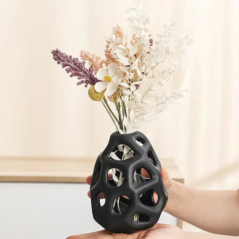 Black ceramic vase with geometric cutouts holding dried flowers featuring nordic classical design by decorbites