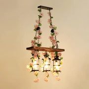 A rustic wooden cage island pendant light with black metal lanterns and pink plant decoration for restaurant lighting