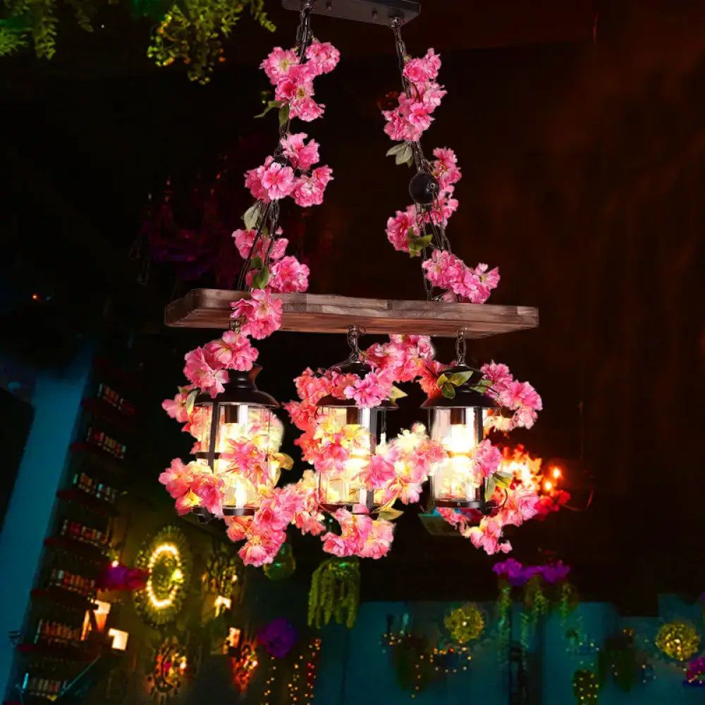 A rustic wooden chandelier with three glowing clear glass heads restaurant island lanterns and vibrant pink flower decor