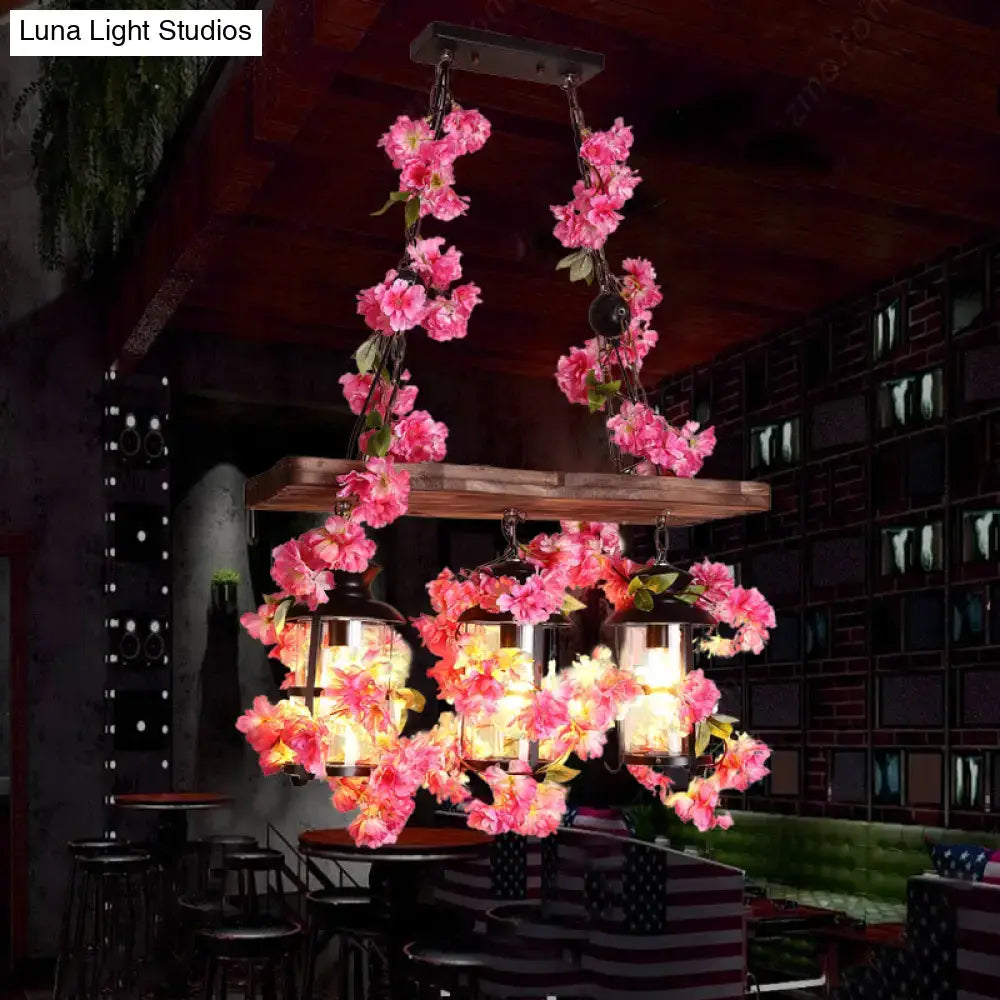 A rustic wooden chandelier with vibrant pink flowers and clear glass hanging lanterns as a restaurant island light with three cylindrical heads