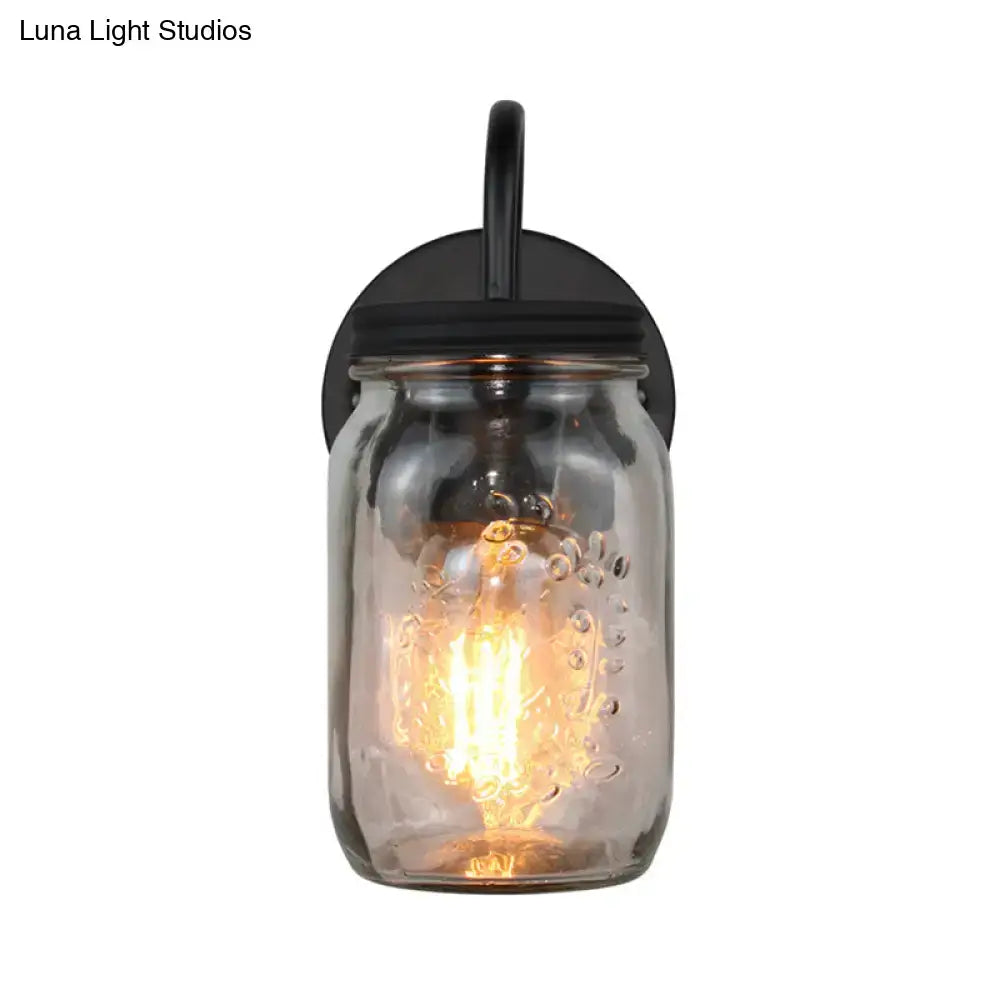 A rustic black metal wall lamp with clear glass black jar shade and exposed filament bulb for bedroom light