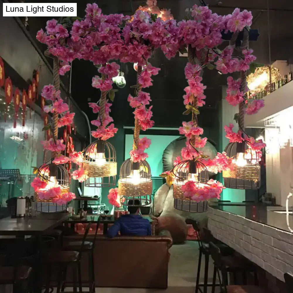 Pink artificial cherry blossom vines drape over industrial metal black island pendant ceiling lamps with ornate cage fixture height