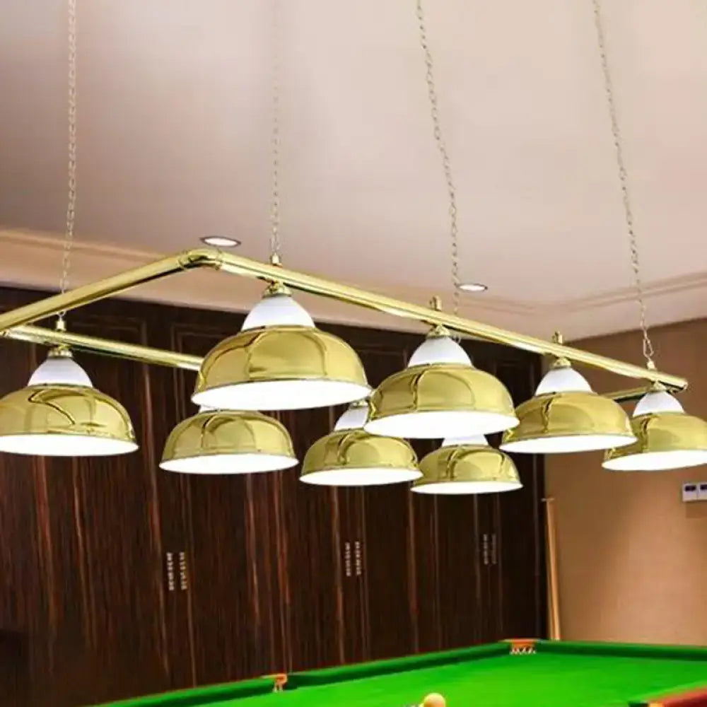 Gold-colored metal mirrored bowl pendant lights with white interiors suspend from brass bar over billiard table
