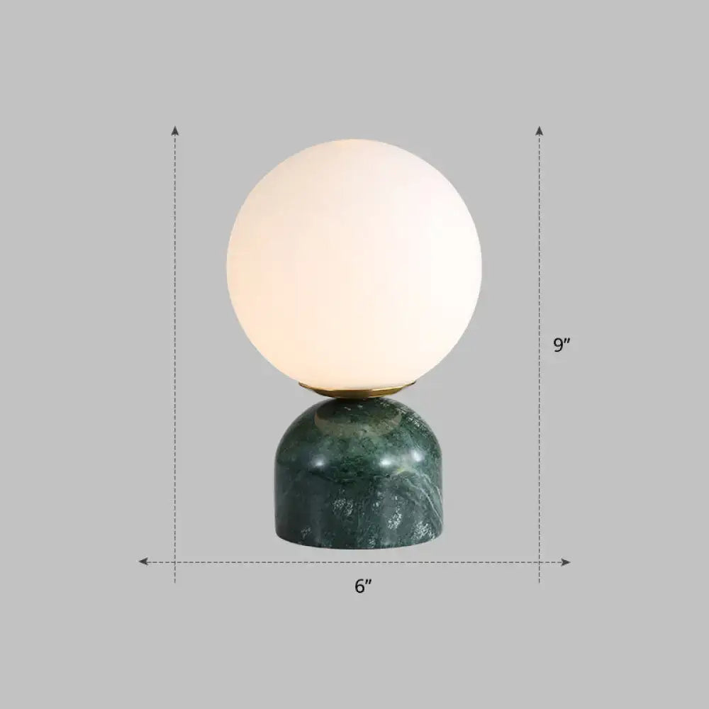 Decorbites™ ivory glass nightstand light with a glowing spherical shade on a dark green marble pedestal for 110v-120v use