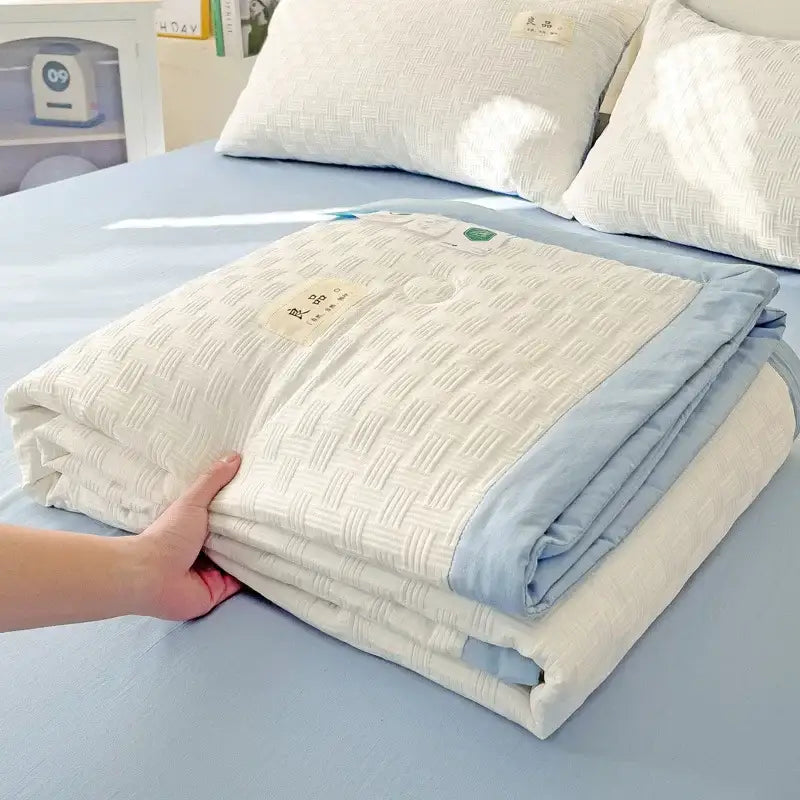 A neatly folded cream jacquard summer cool blanket with light blue piping and embroidered labels by decorbites