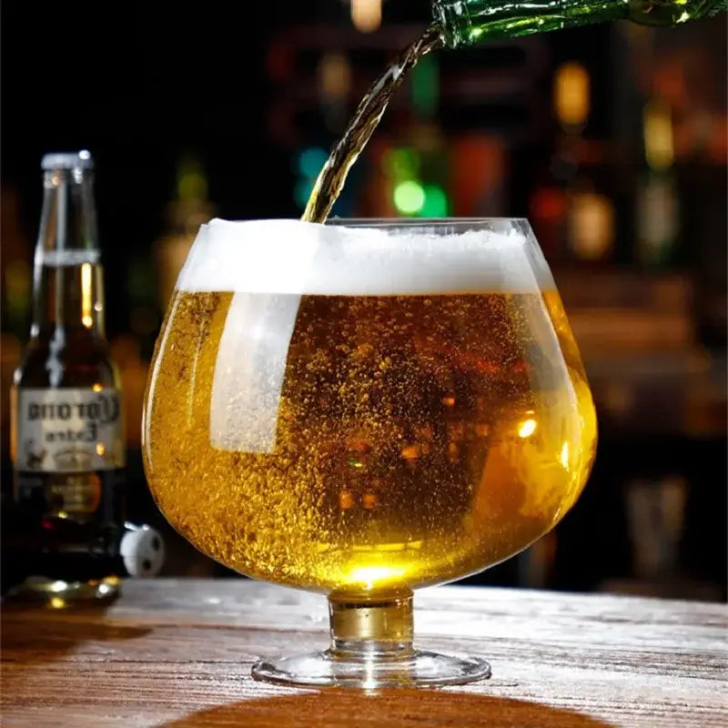 Golden beer with frothy white head poured into clear stemmed glass in decorbites jumbo party large capacity goblet
