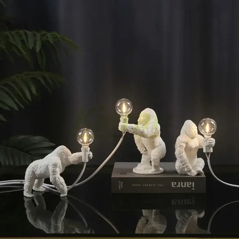 Three white resin gorilla figurines holding lit bulbs connected by cords decorbites king kong led desk lamp for living room