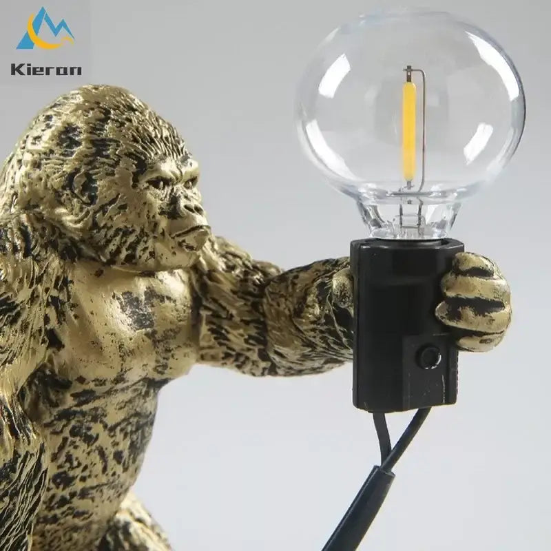 Golden gorilla figurine holding clear glass bulb with exposed filament in decorbites king kong led black resin desk lamp