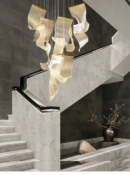 Modern gold-toned metallic led ceiling chandelier with wave-like sculptural elements above marble staircase for living room