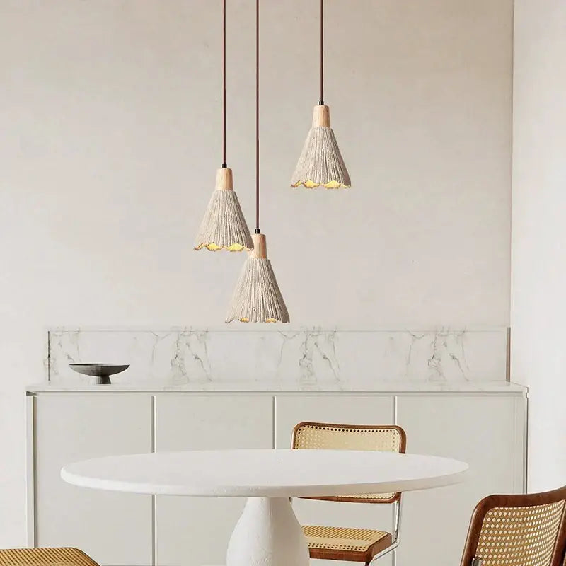Three beige woven tassel pendant lamps with wooden tops hanging above a white table in decorbites led cement style
