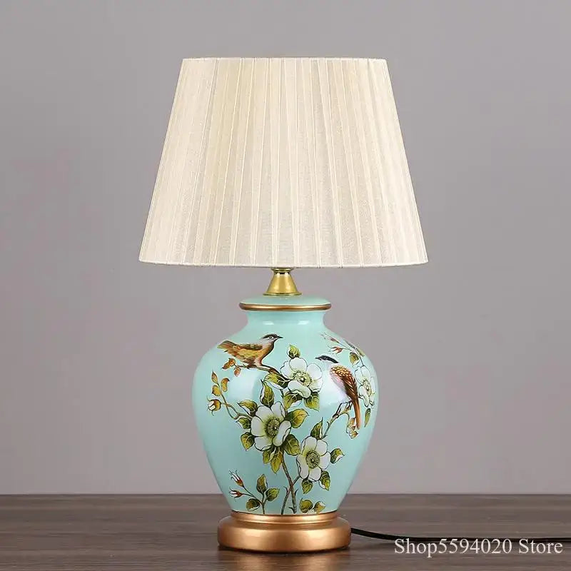 A light blue decorbites led ceramic table lamp with hand-painted birds and flowers topped with a cream pleated shade