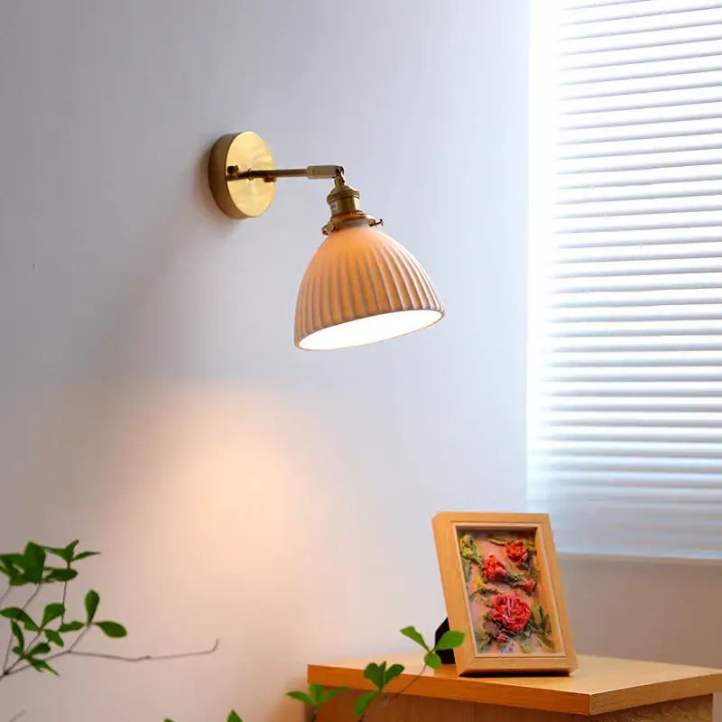 A vintage-style brass decorbites led ceramic wall sconce with ribbed off-white shade for bedroom or bathroom lighting