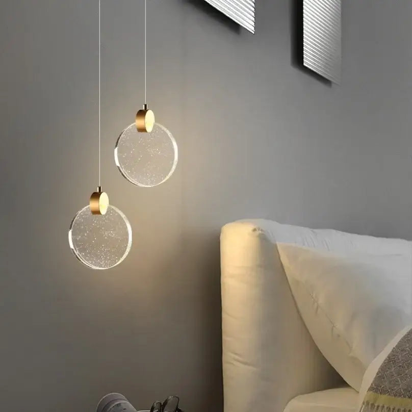 Two gold-toned decorbites™ led crystal pendant lights with clear glass shades hang against a gray wall