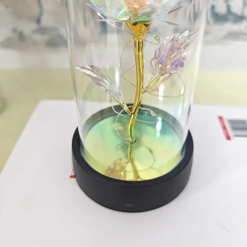 A golden iridescent glass eternal rose light with delicate petals in a clear dome on a black base for weddings