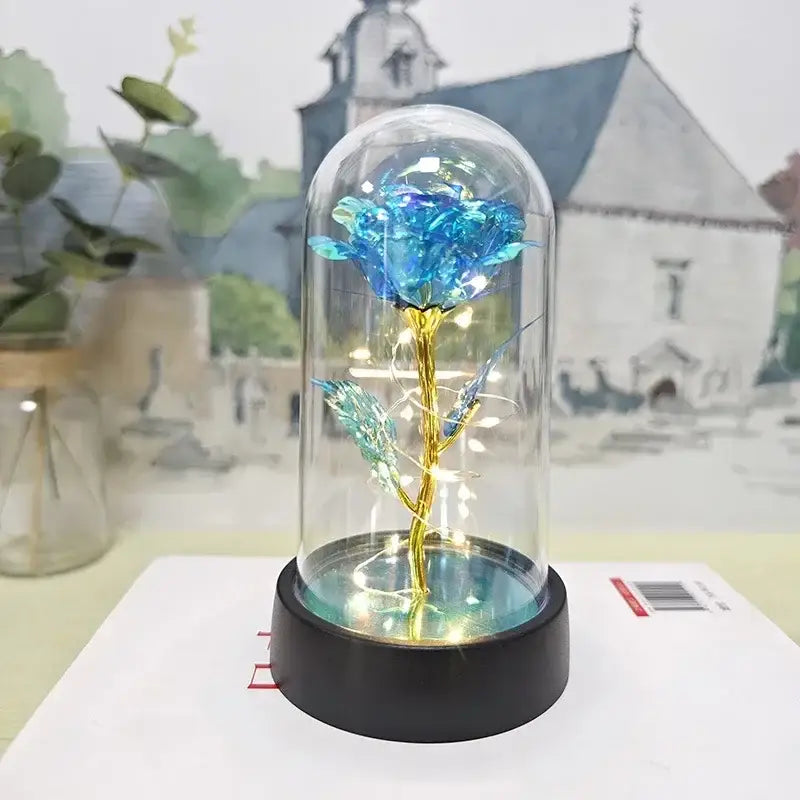 A glowing blue eternal rose light with a golden stem inside a glass dome illuminated by led lights for decorbites