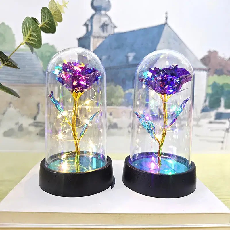 Two iridescent purple DecorBites™ eternal rose lights with golden stems and blue leaves under glass domes for weddings