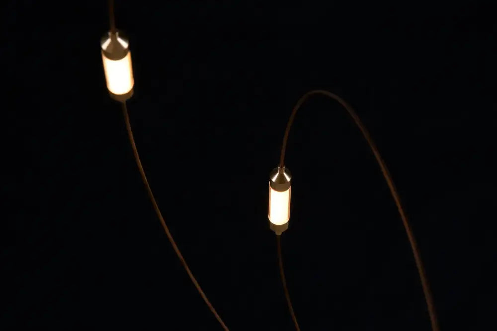 Two warm cylindrical led firefly chandelier pendant lights with metallic caps in engineering minimal design hanging against black background