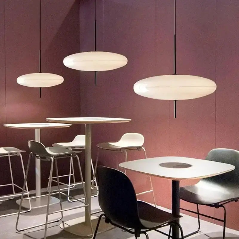 Modern white oval DecorBites LED flying saucer pendant lights with black cords hang above minimalist café tables