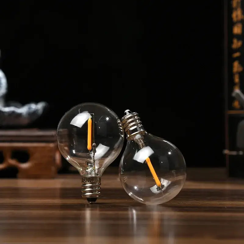 Two clear glass decorbites led g40 e12 bulbs with orange led filaments and metallic screw bases for outdoor garden decor
