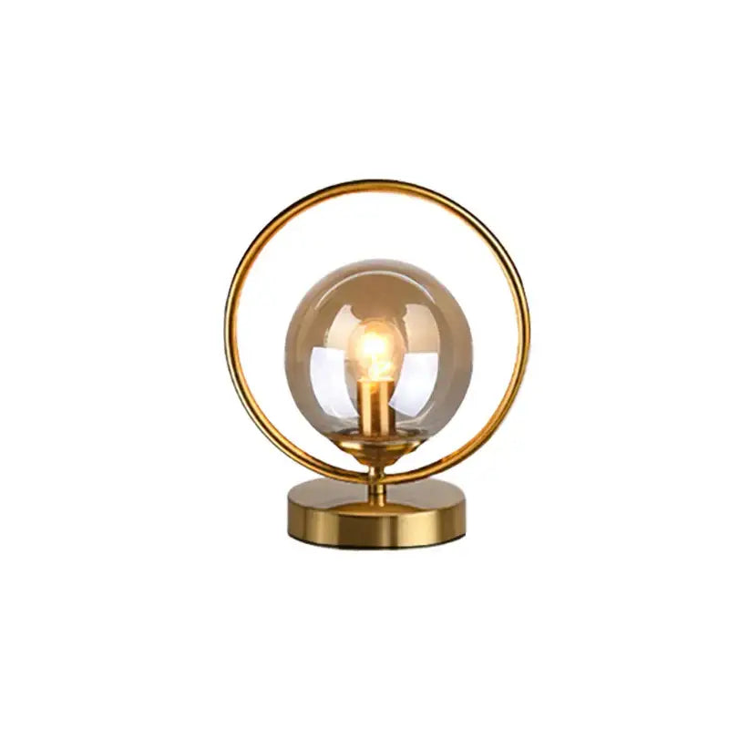 Gold-toned decorbites led glass table lamp with brass ring and smoked glass globe housing an exposed bulb