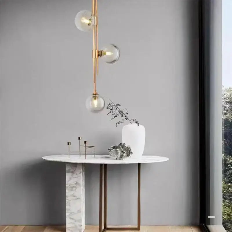 A modern minimalist console table with white marble top and gold-toned legs under decorbites led glass ball pendant light